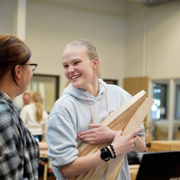 Een student die lacht en delen van haar meubel in haar armen heeft.