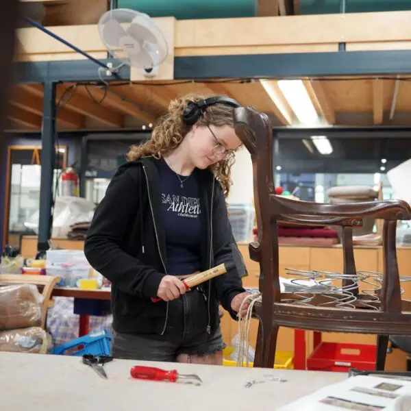 Een student van het Hout en Meubileringscollege timmert een spijker in een stoel.