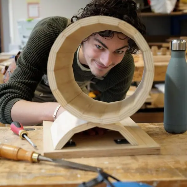 Een student van het Hout en Meubileringscollege kijkt door de ronde vorm van zijn meubel