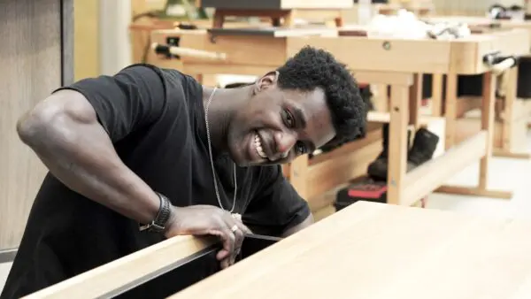 Student kijkt lachend in de camera, zijn hand leunt op een houten lade.