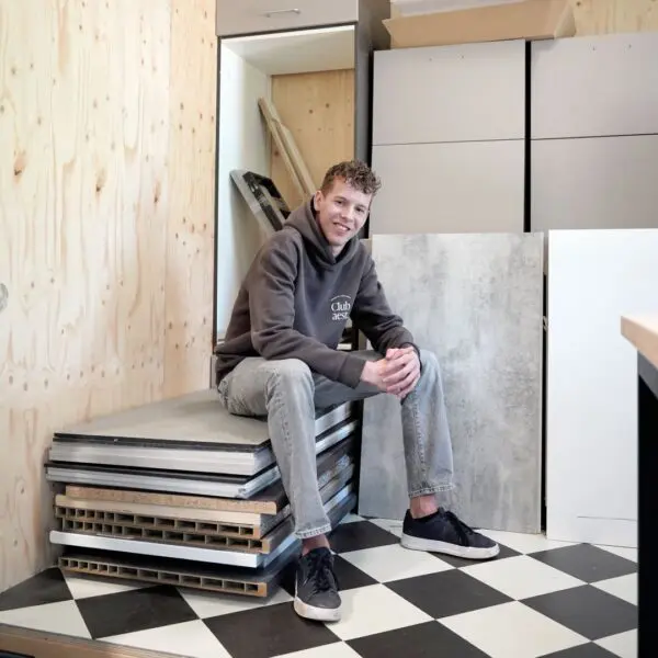 Een student van het Hout en Meubileringscollege die op gestapelde keukendeuren zit.
