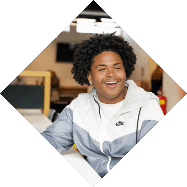 Jongen met afrokapsel en Nikejasje kijkt lachend in de camera