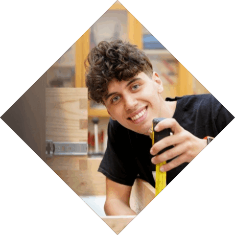 Student heeft een rolmaat in zijn hand en meet een laatje, kijkt lachend in de camera