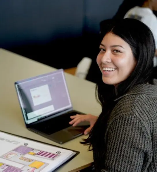 Student is aan het werk op laptop en heeft tekeningen liggen