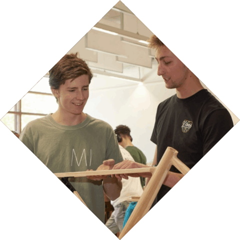 2 studenten kijk naar een werkstuk en voelen aan hout